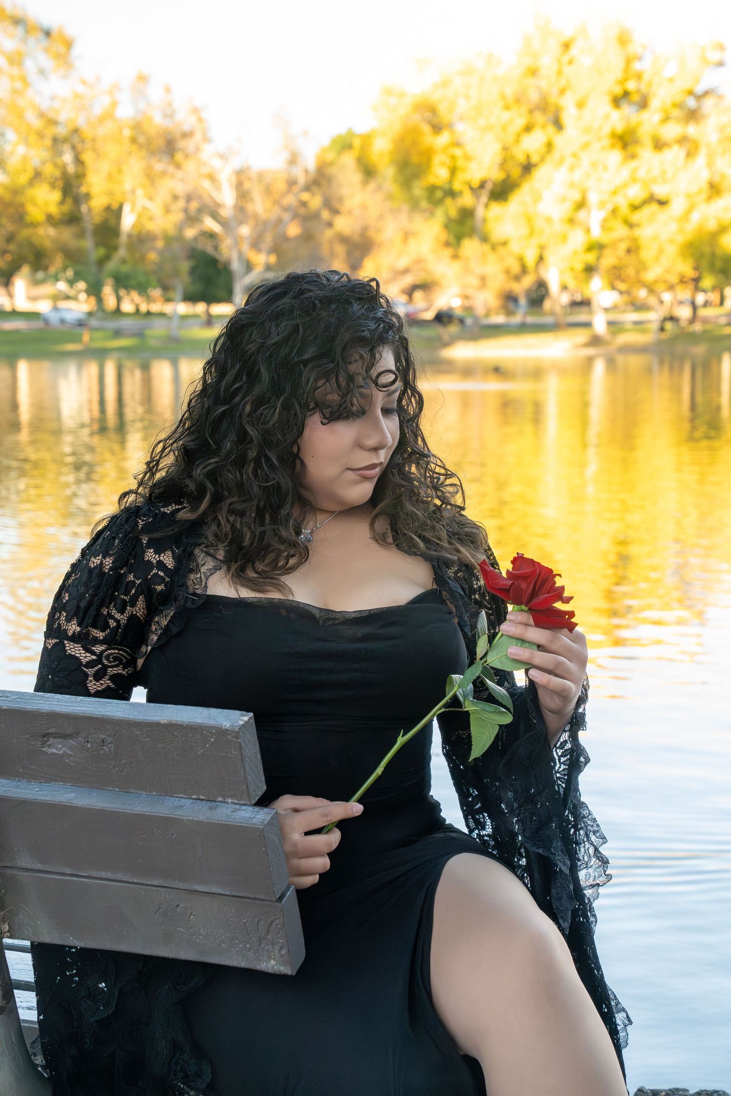 A series of romantic photos by a lake showing someone in a black lace dress holding a red rose at sunset.
