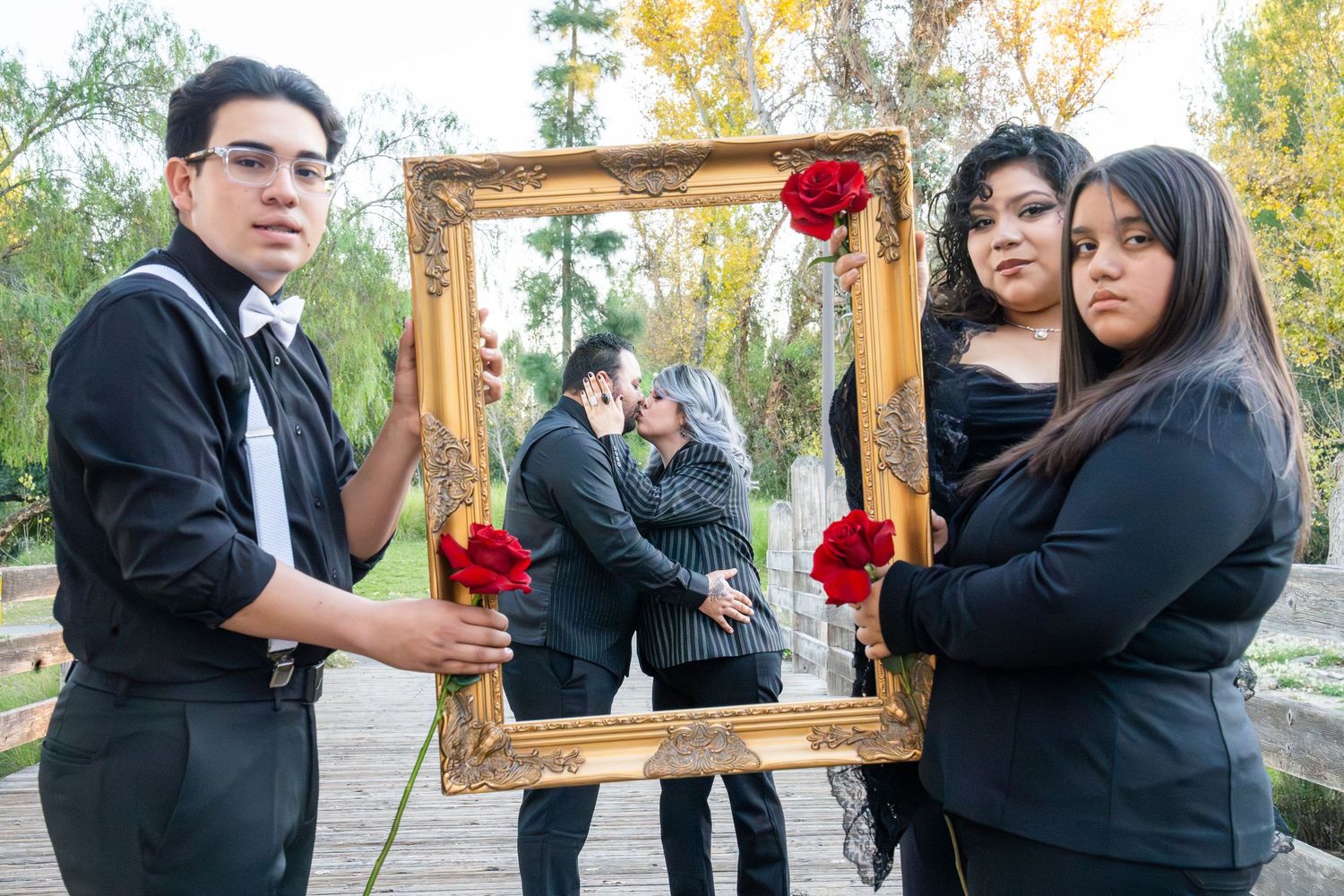 A group poses with a decorative gold frame adorned with red roses in an outdoor setting during autumn.