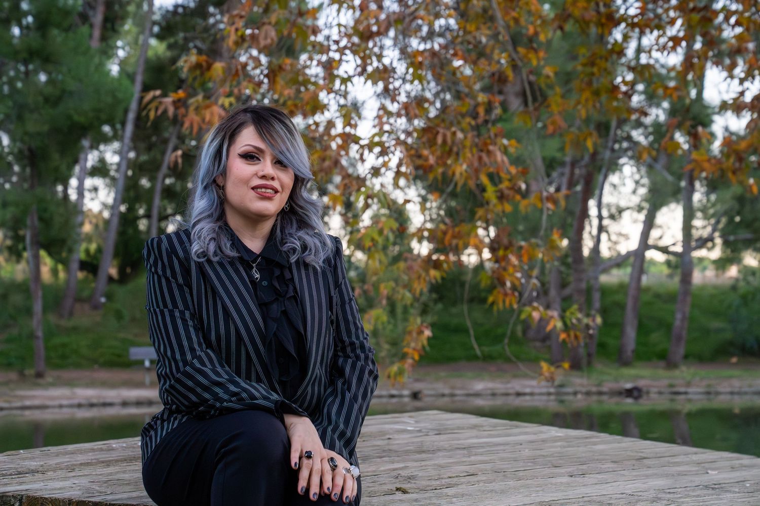 A person in a striped blazer sits on stone steps surrounded by autumn foliage in an outdoor setting.