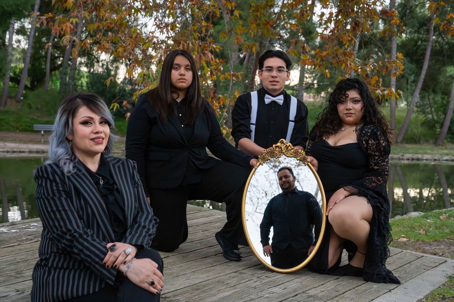 A group photo session in formal black attire taken outdoors with autumn trees in the background.