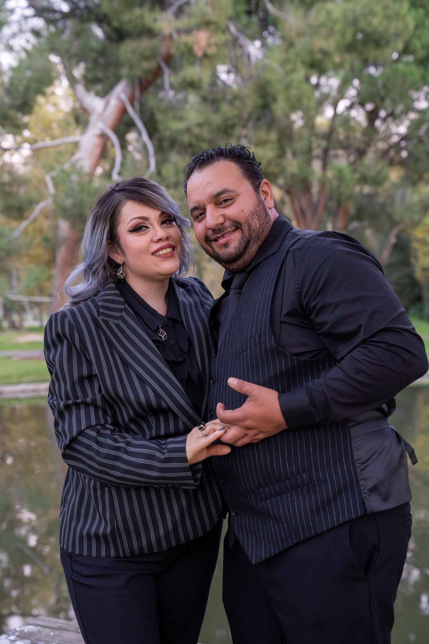 A couple shares playful candid moments together outdoors in coordinating striped outfits near trees.
