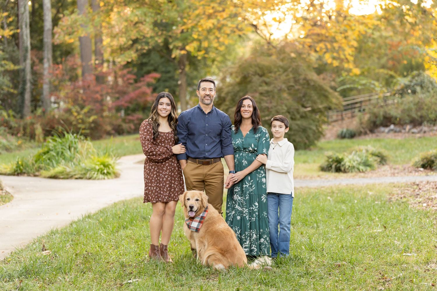 A group poses outdoors on a grassy hill during autumn with golden sunlight and fall foliage in the background.