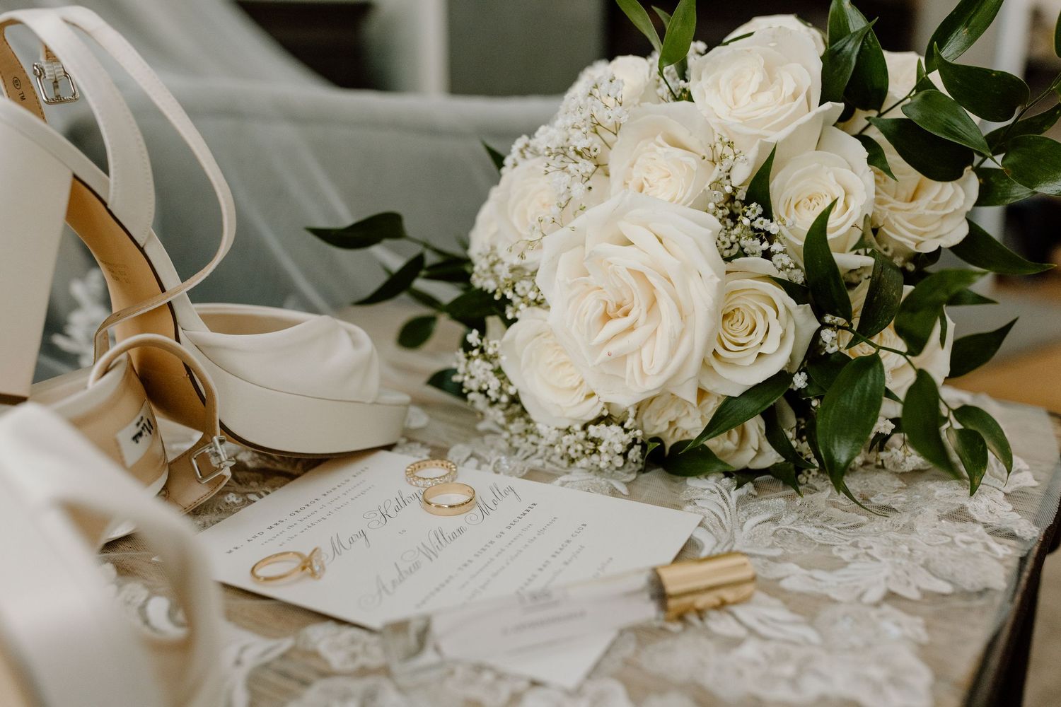 Wedding rings rest on handwritten vows with white roses and greenery decorating an elegant table setting.