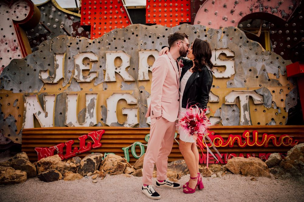 A couple shares a romantic dance moment in front of a rustic wall decorated with vintage signage and string lights.