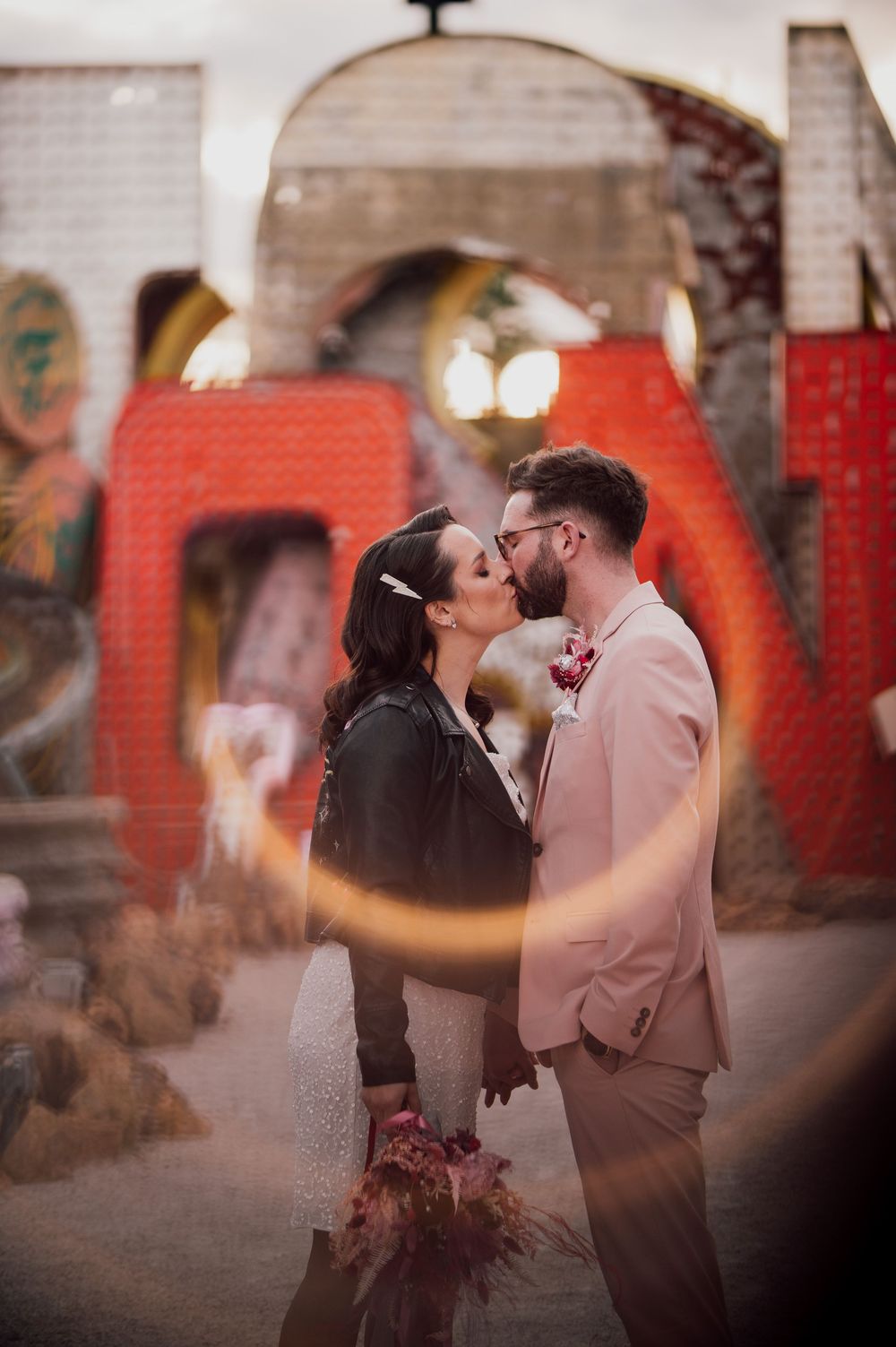 A romantic couple sharing a tender moment in front of a blurred red background at dusk.