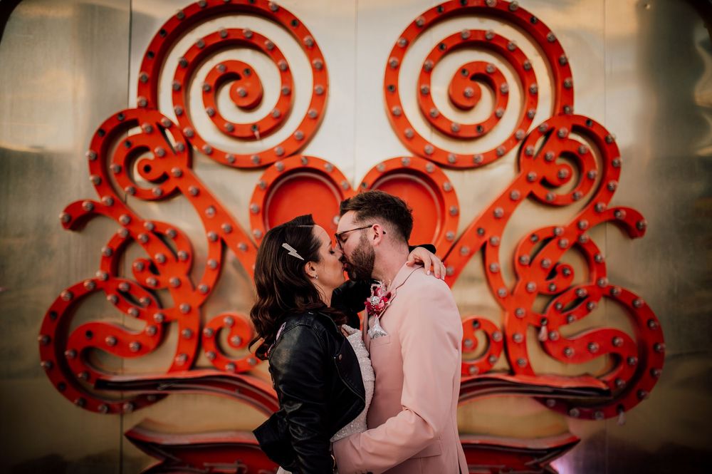A romantic couple shares an intimate moment in front of a large red spiral wall art installation.