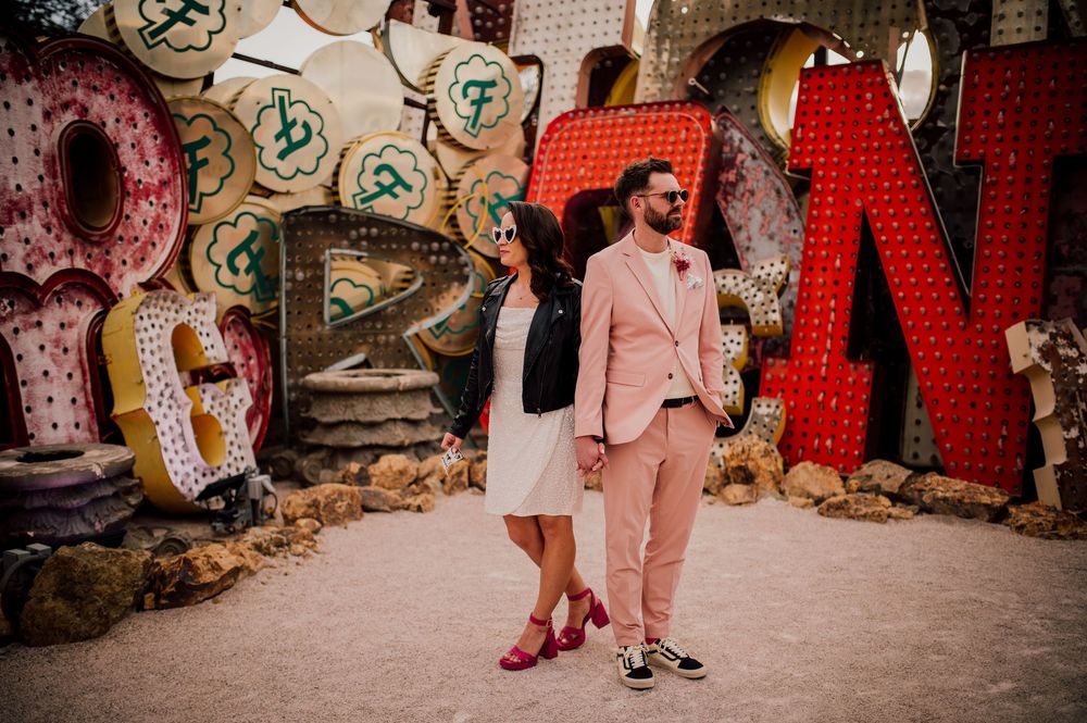 A couple poses in front of colorful graffiti letters wearing coordinated pink outfits and red shoes.