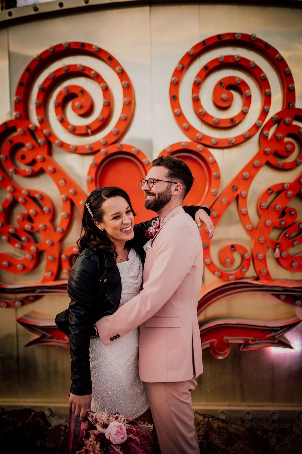 A couple shares intimate moments in front of red spiral decorative wall art at their wedding celebration.