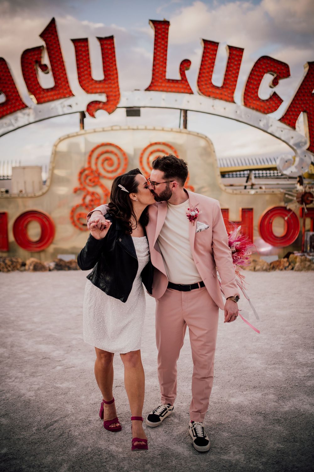 A couple shares a romantic moment under a vintage Lady Luck sign at an old amusement park.