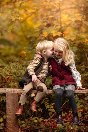 Two children sitting together on wooden log in autumn forest setting.