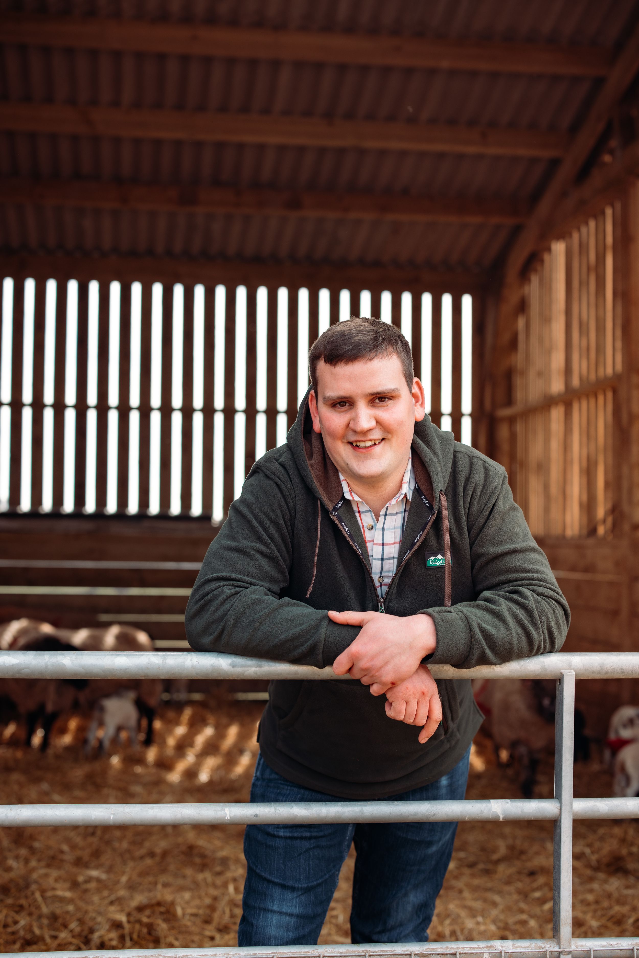 Young man in casual attire leaning on metal railing in rustic barn setting.