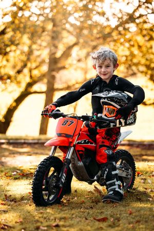 Child playing with red dirt bike on fallen autumn leaves during golden hour.