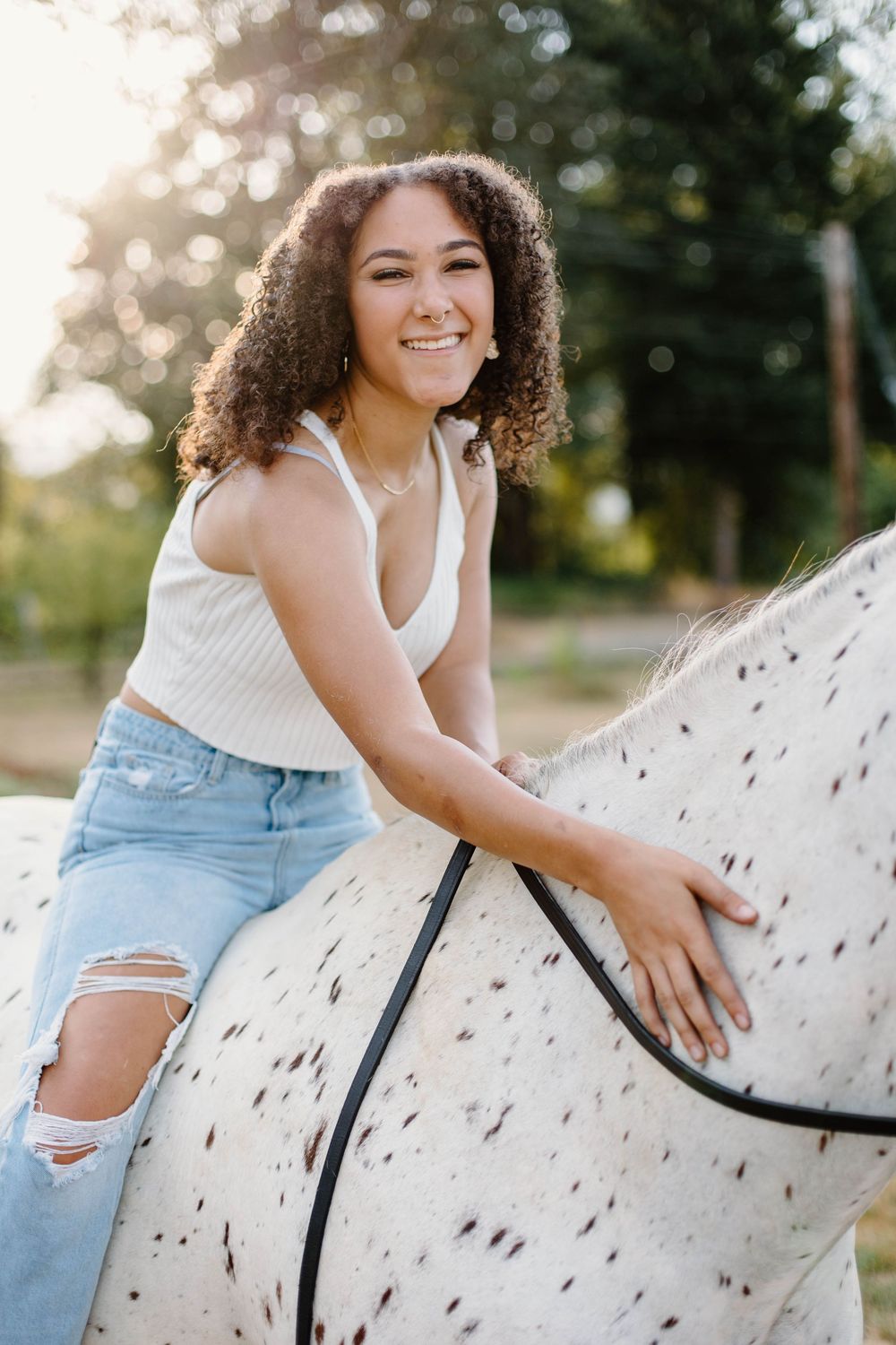 Joyful summer photoshoot with a spotted white horse in golden sunlight.
