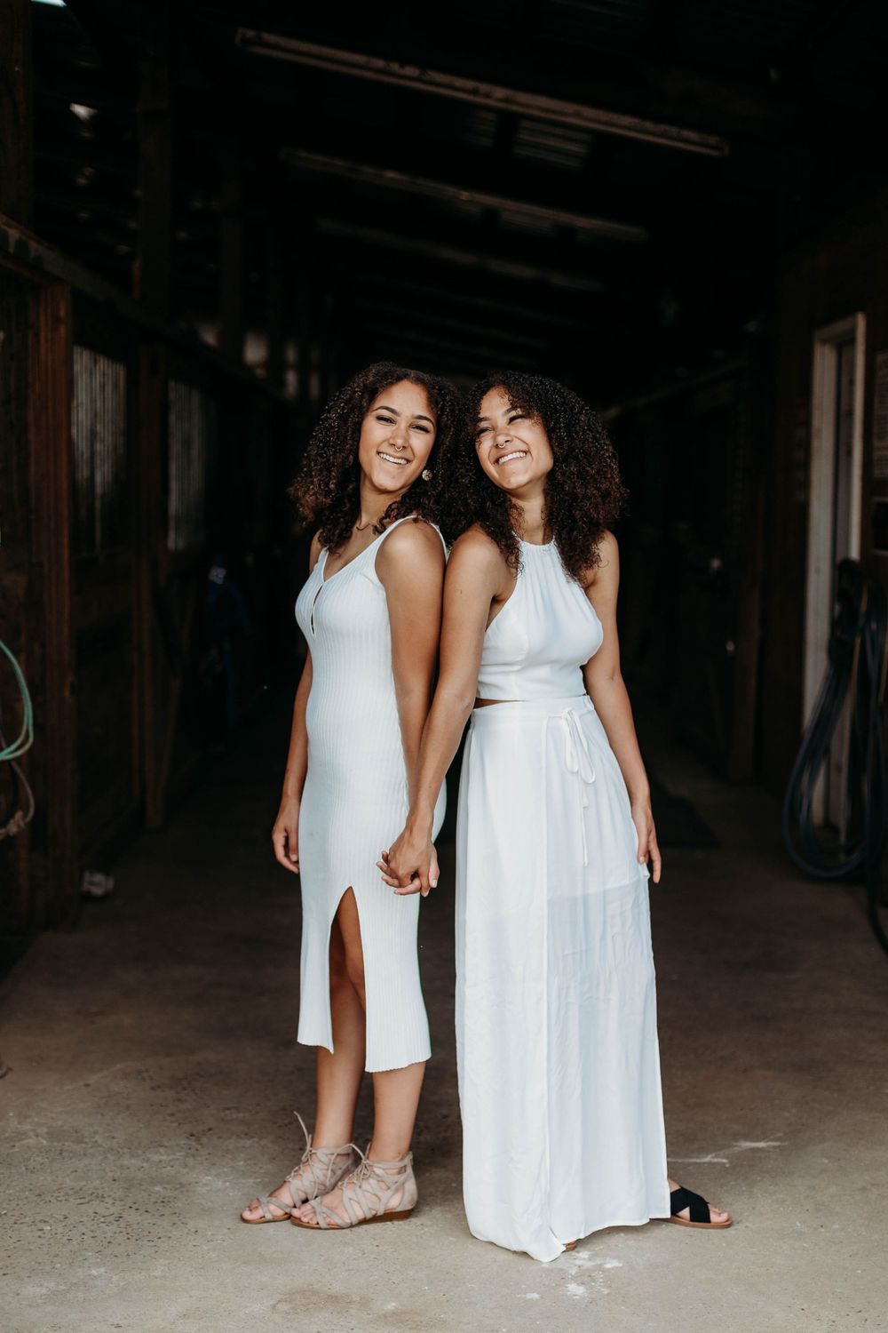 Two people in white dresses holding hands in a dimly lit indoor space.