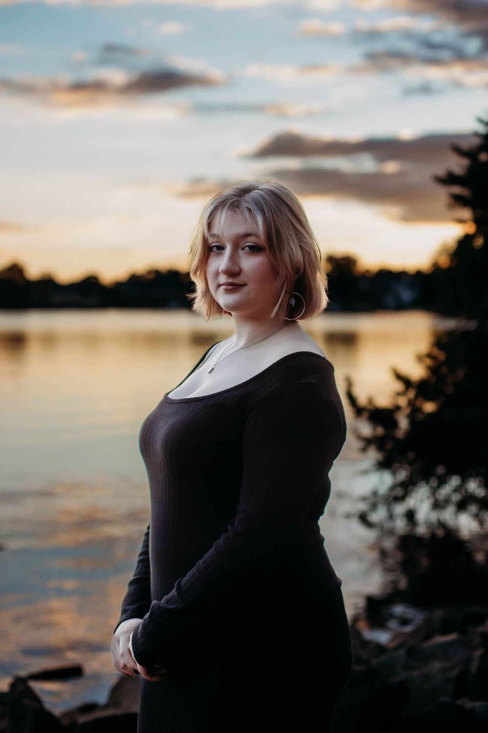 Silhouette portrait against sunset sky over water with warm golden lighting.