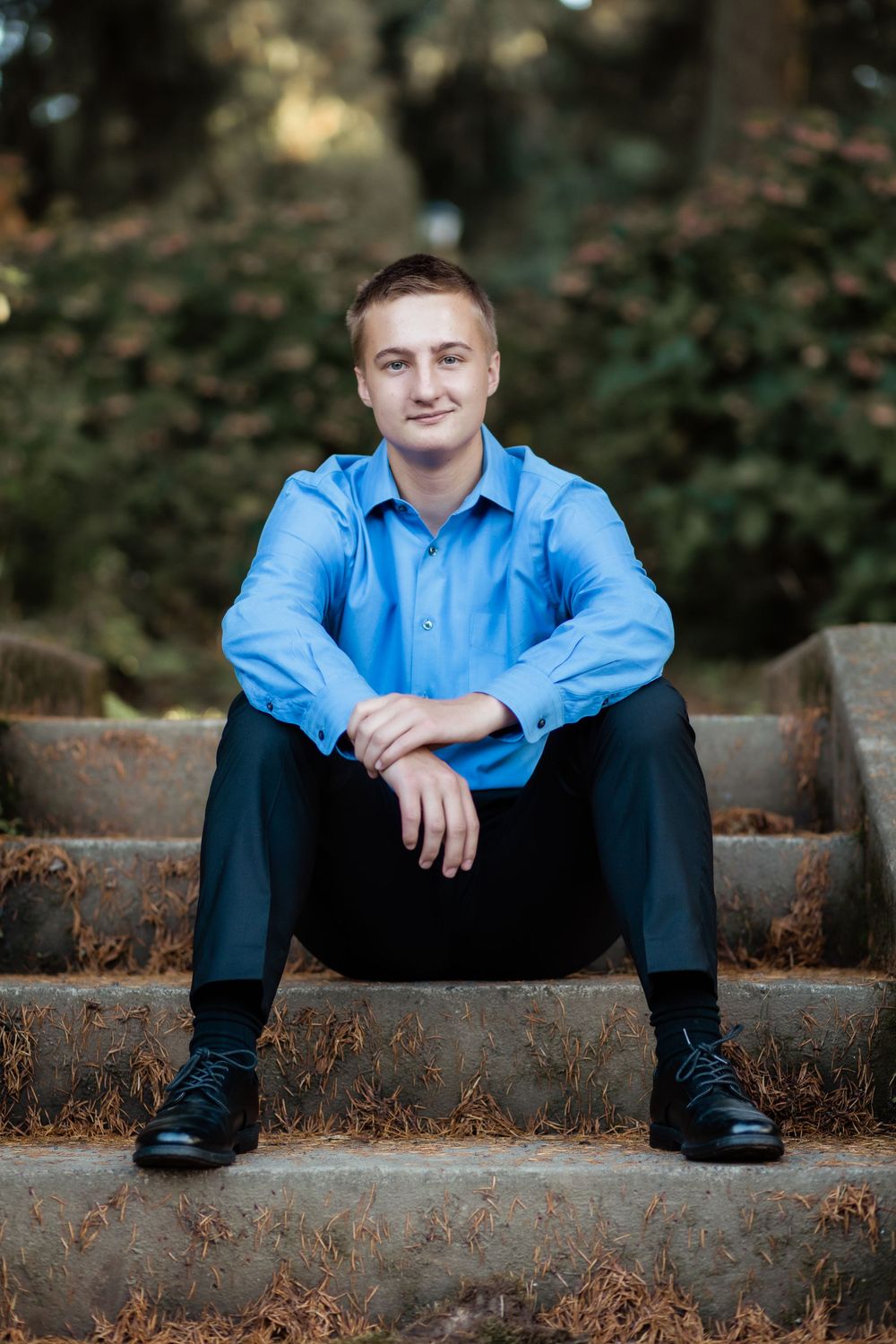 Person in blue button-down shirt sitting on concrete steps during fall season.