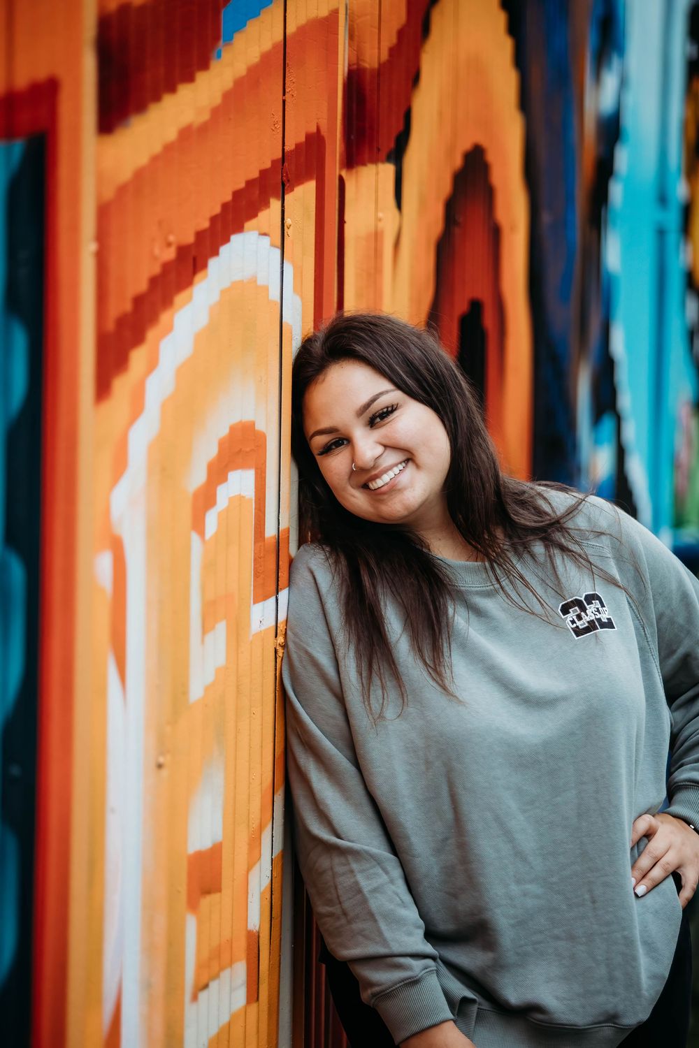 Casual portrait series against colorful orange and blue striped wall wearing grey sweatshirt.