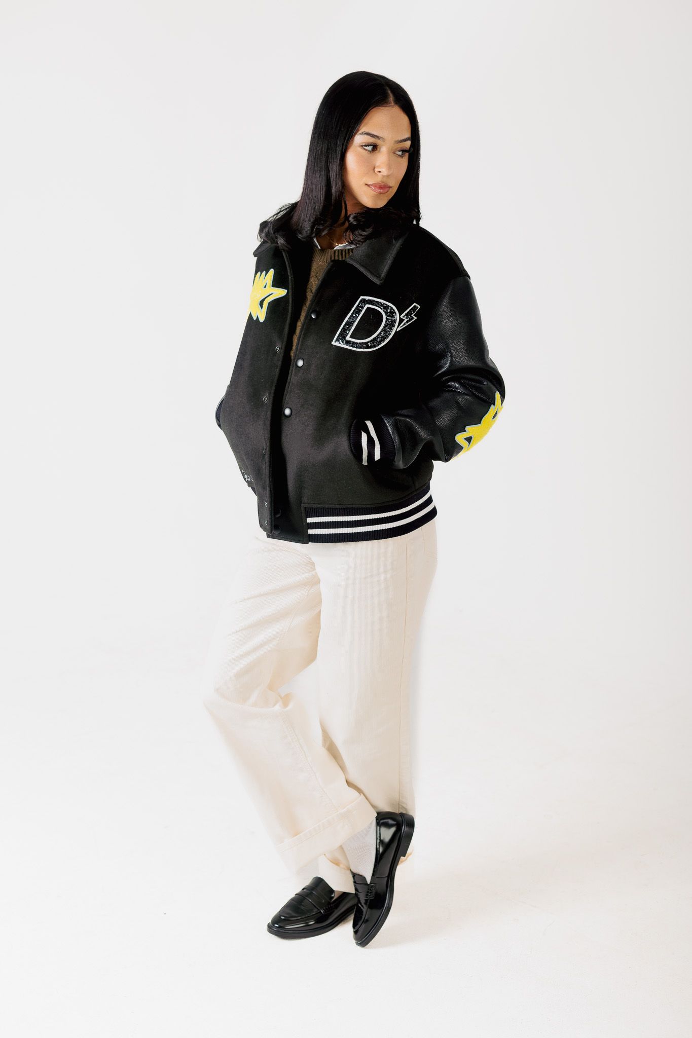 A person wearing a black varsity jacket with white pants poses against a white backdrop in multiple stylish shots.