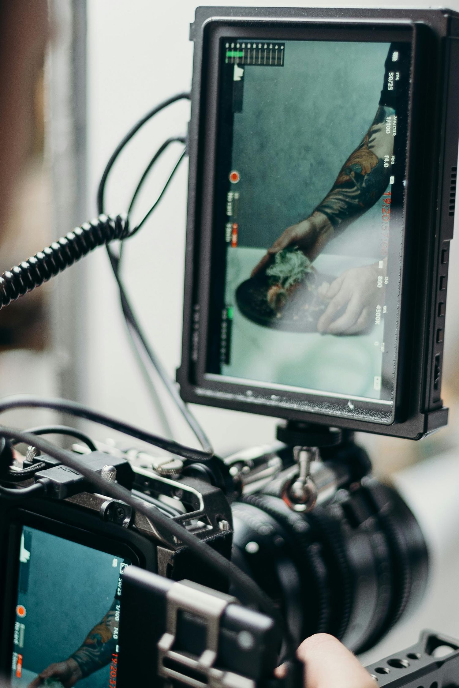 Professional camera monitor displays video feed on set with coiled cables and mounting hardware in dark environment.