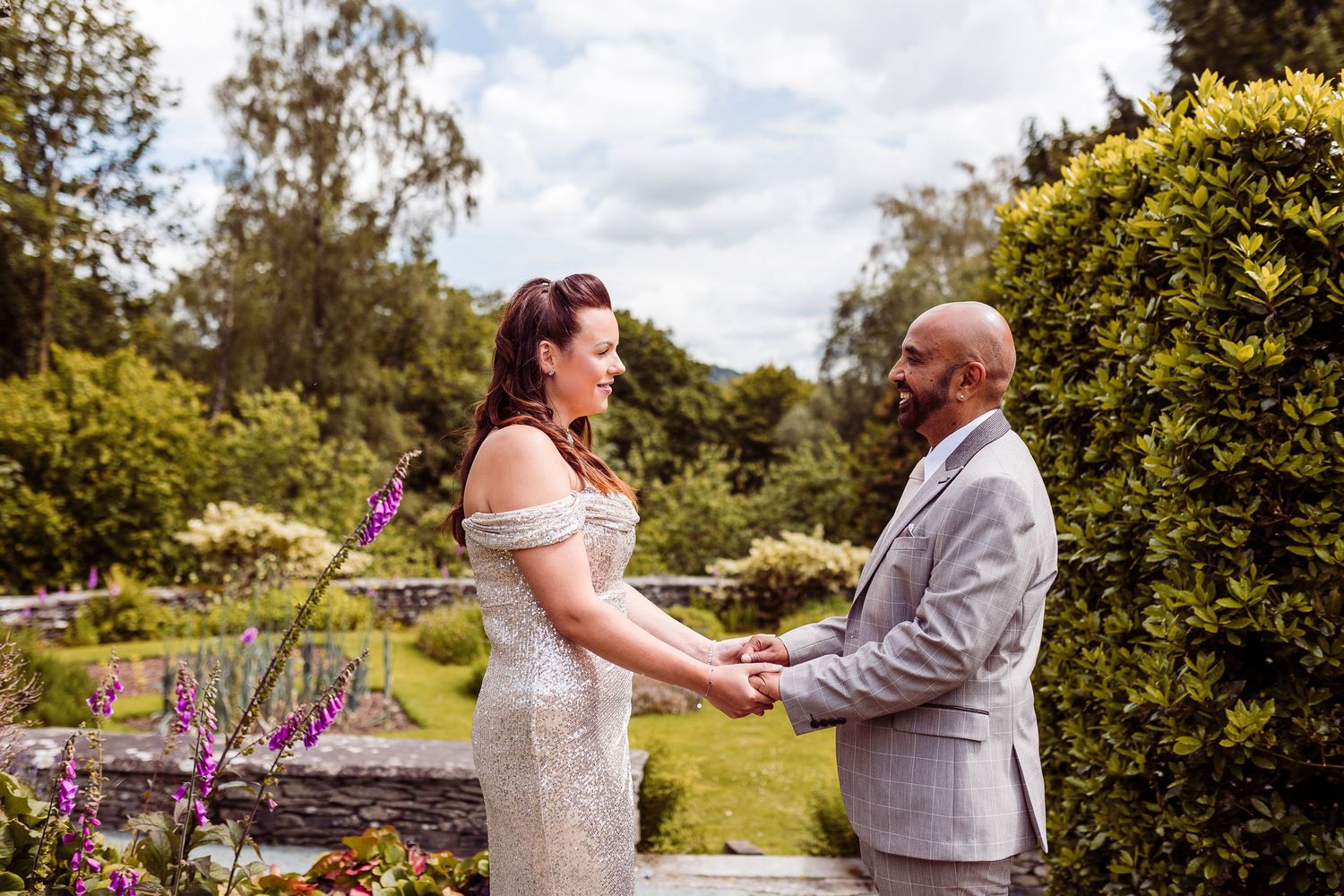 A couple shares a tender moment holding hands in a lush garden setting during their outdoor wedding ceremony.