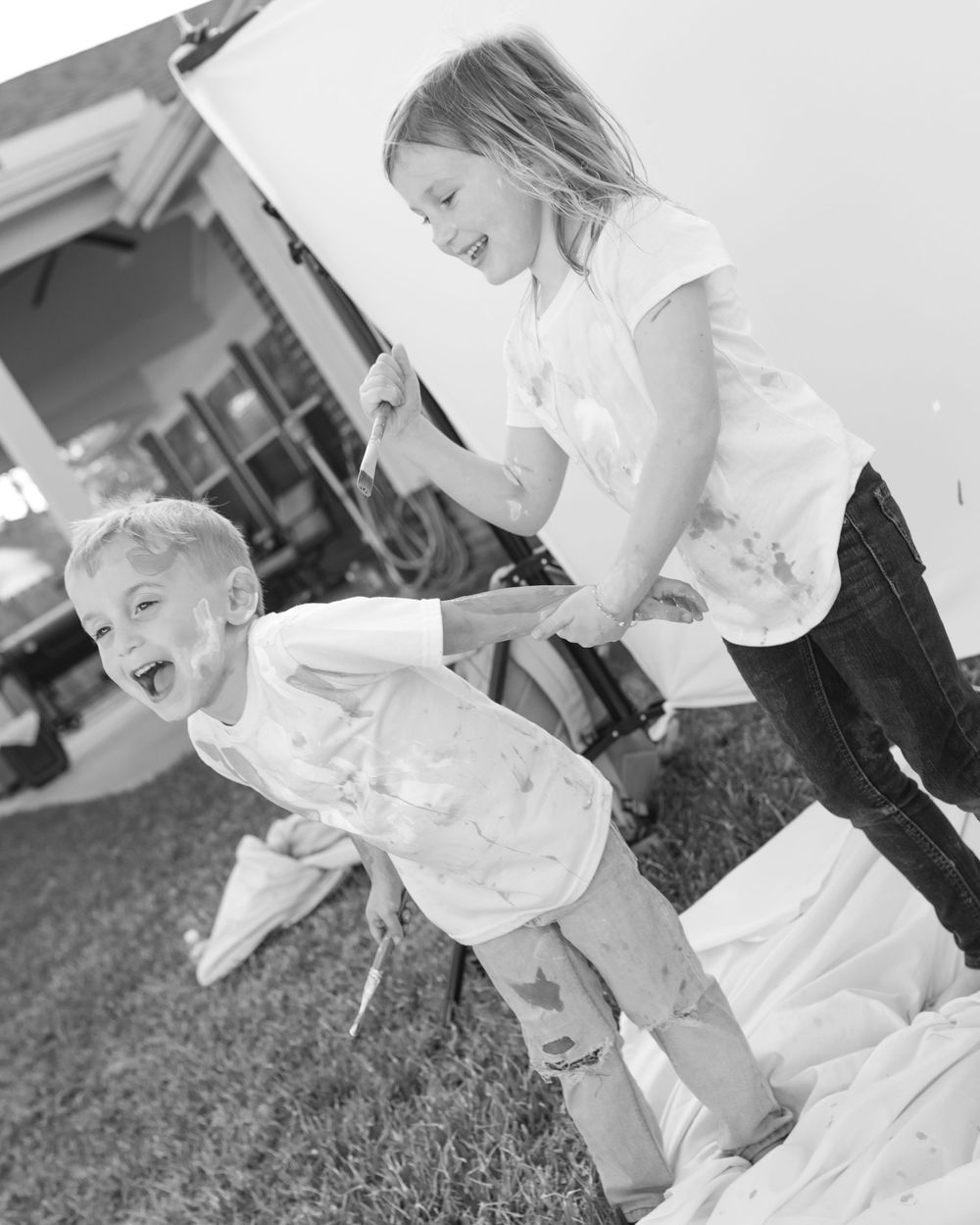 Black and white photos show children in white outfits playing and laughing together outdoors on grass.