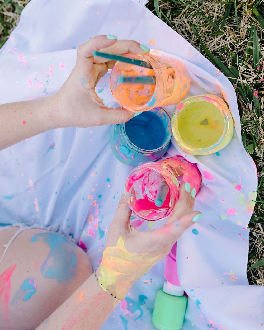 Colorful paint pots and messy paint splatters on white paper create a vibrant artistic workspace scene.