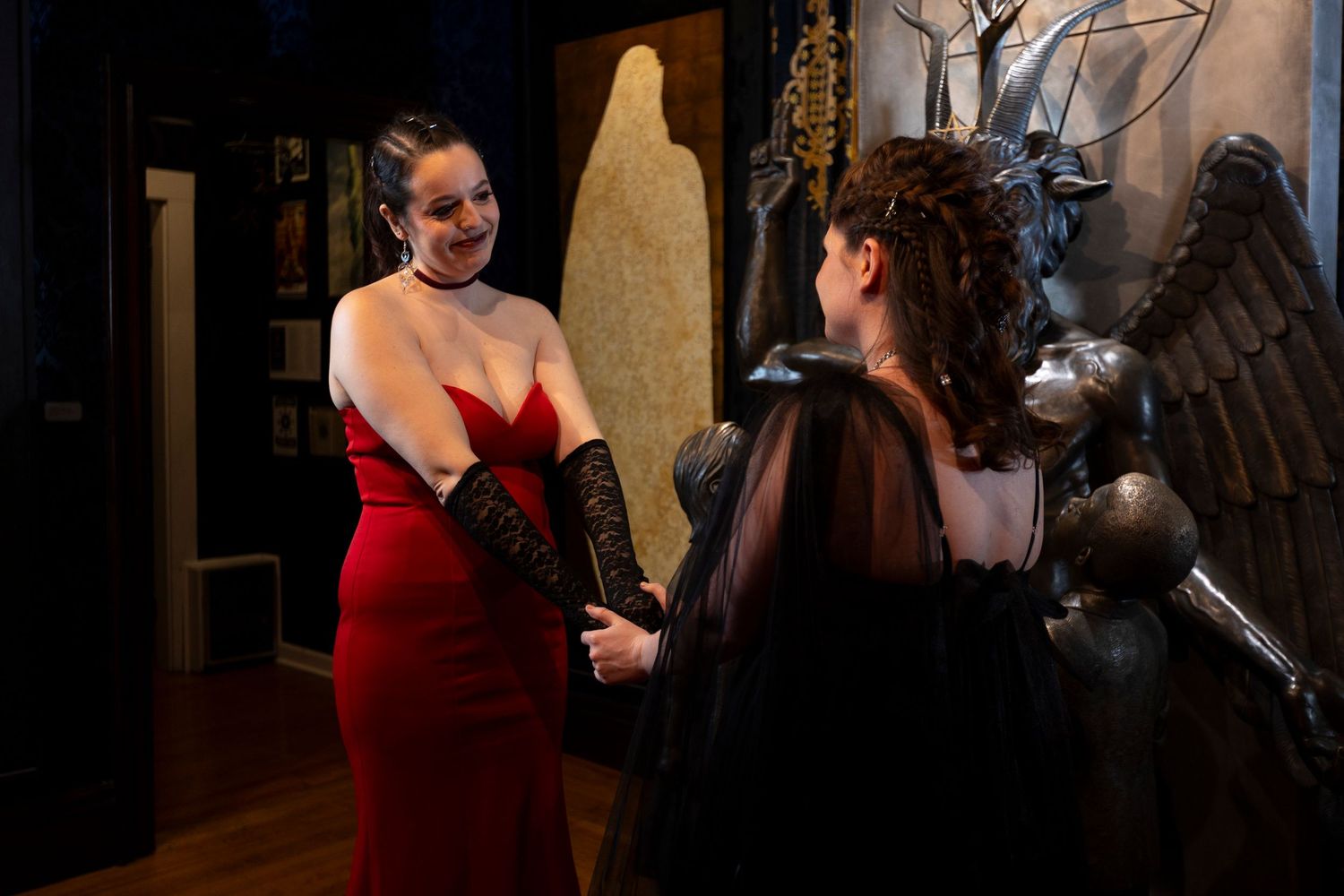 A person in a red dress walks through a dimly lit hallway with ornate decor and wall sconces.