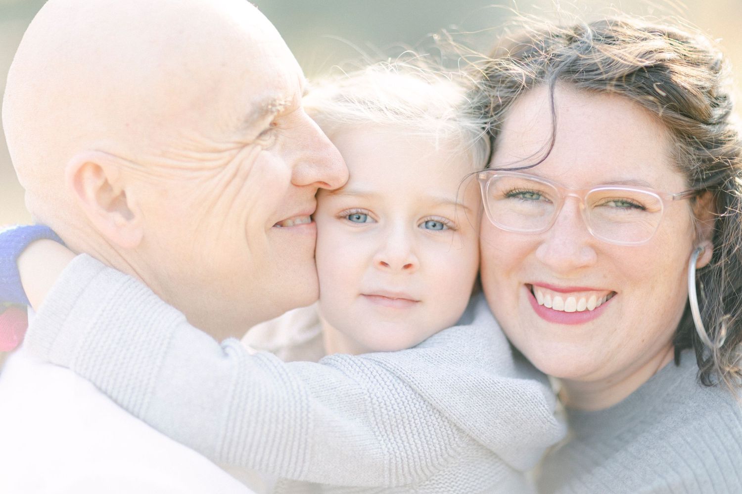 A family sharing a loving embrace while bathed in soft sunlight during an outdoor portrait session.