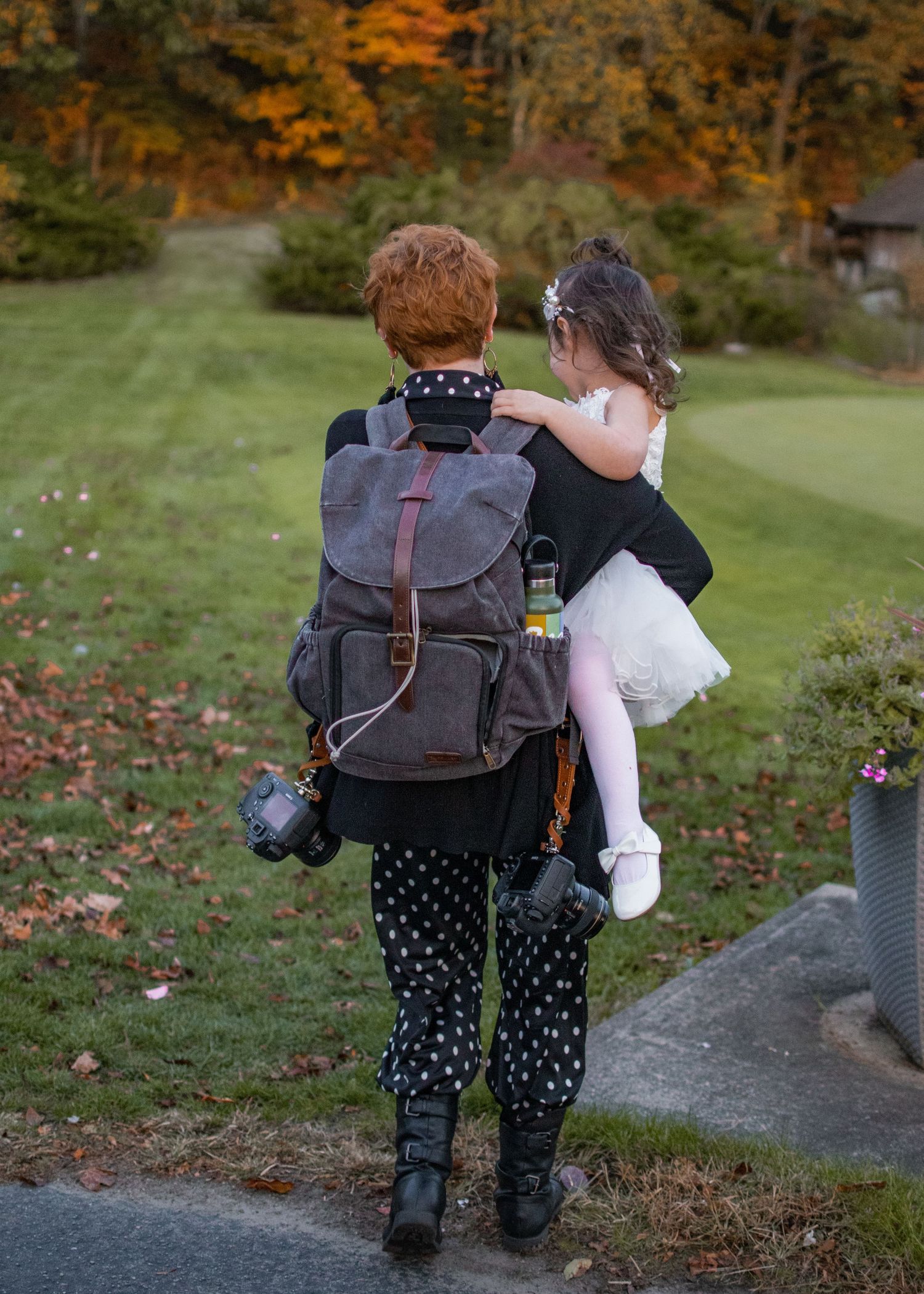 A wedding photographer carries the flower girl with a backpack and two cameras rigged at a wedding.