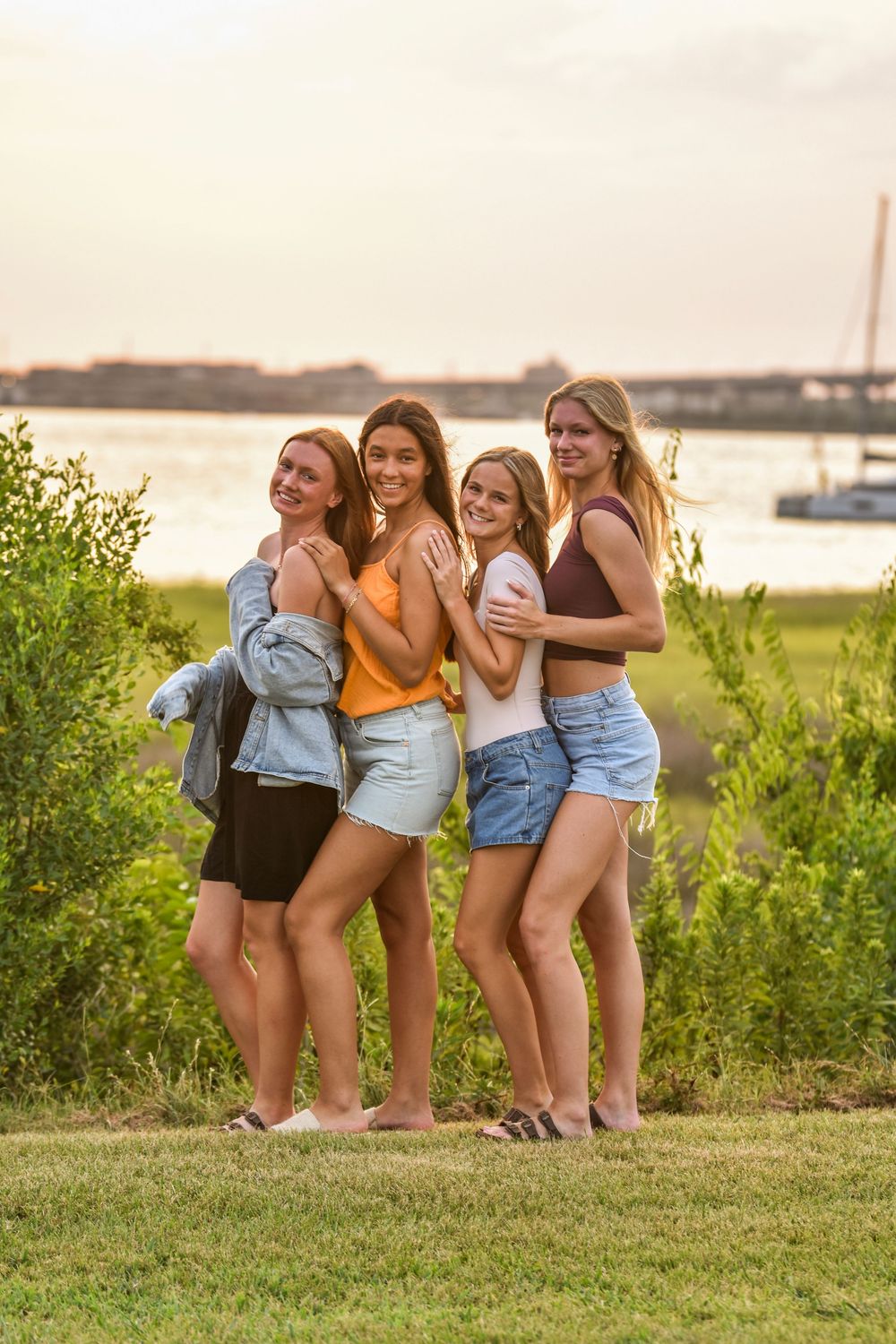 Group of friends in denim shorts enjoying a sunset gathering on grassy hill.