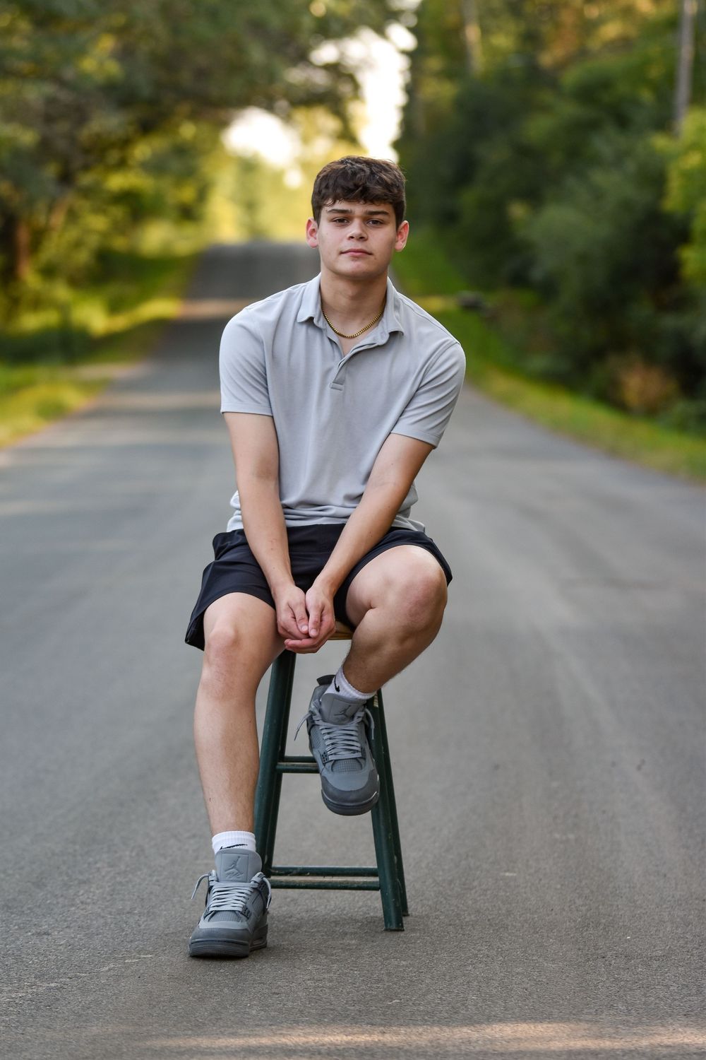 A casual outdoor portrait on a quiet road with someone seated on a dark stool.