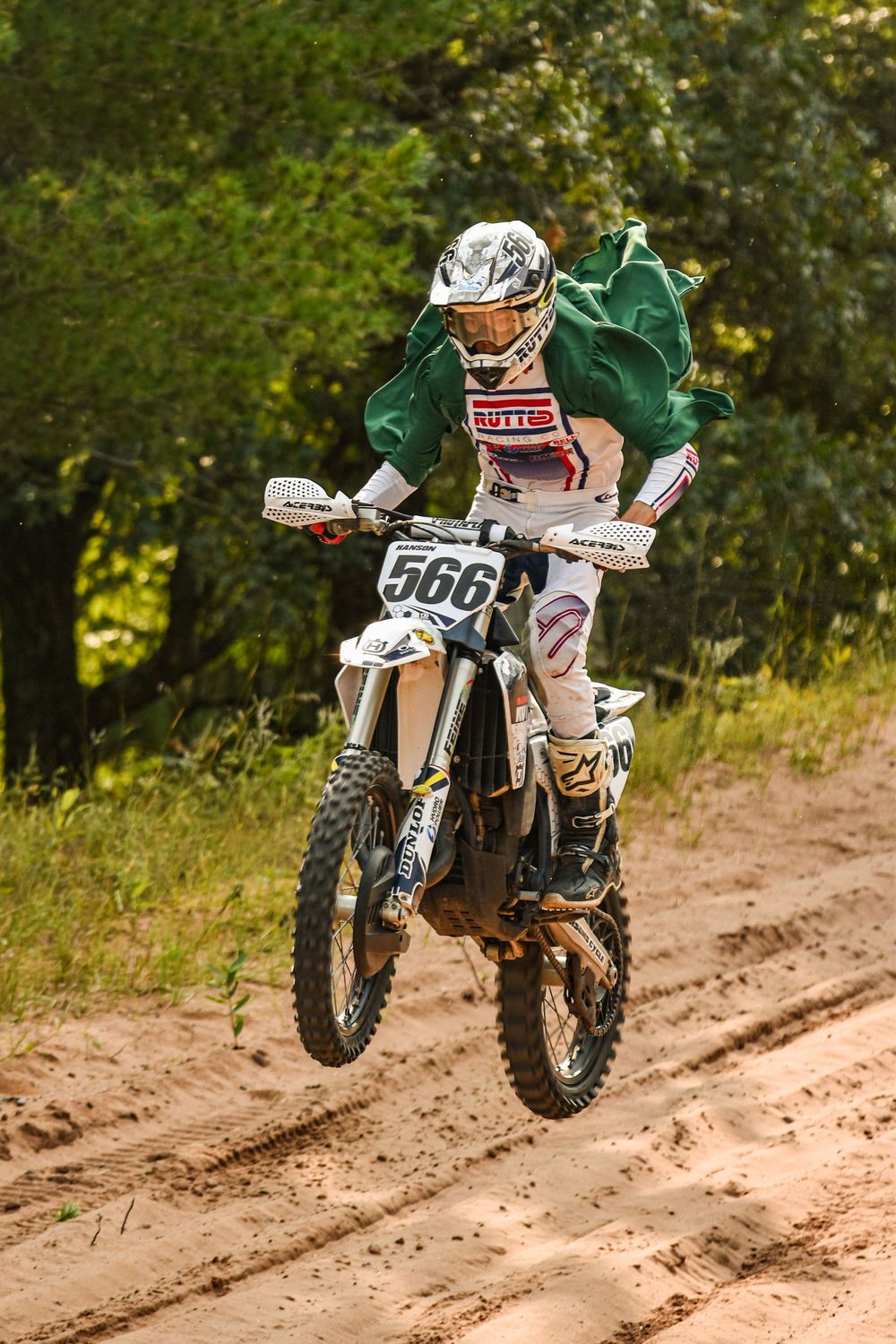 Dirt bike rider jumping over sandy track in green motocross gear.