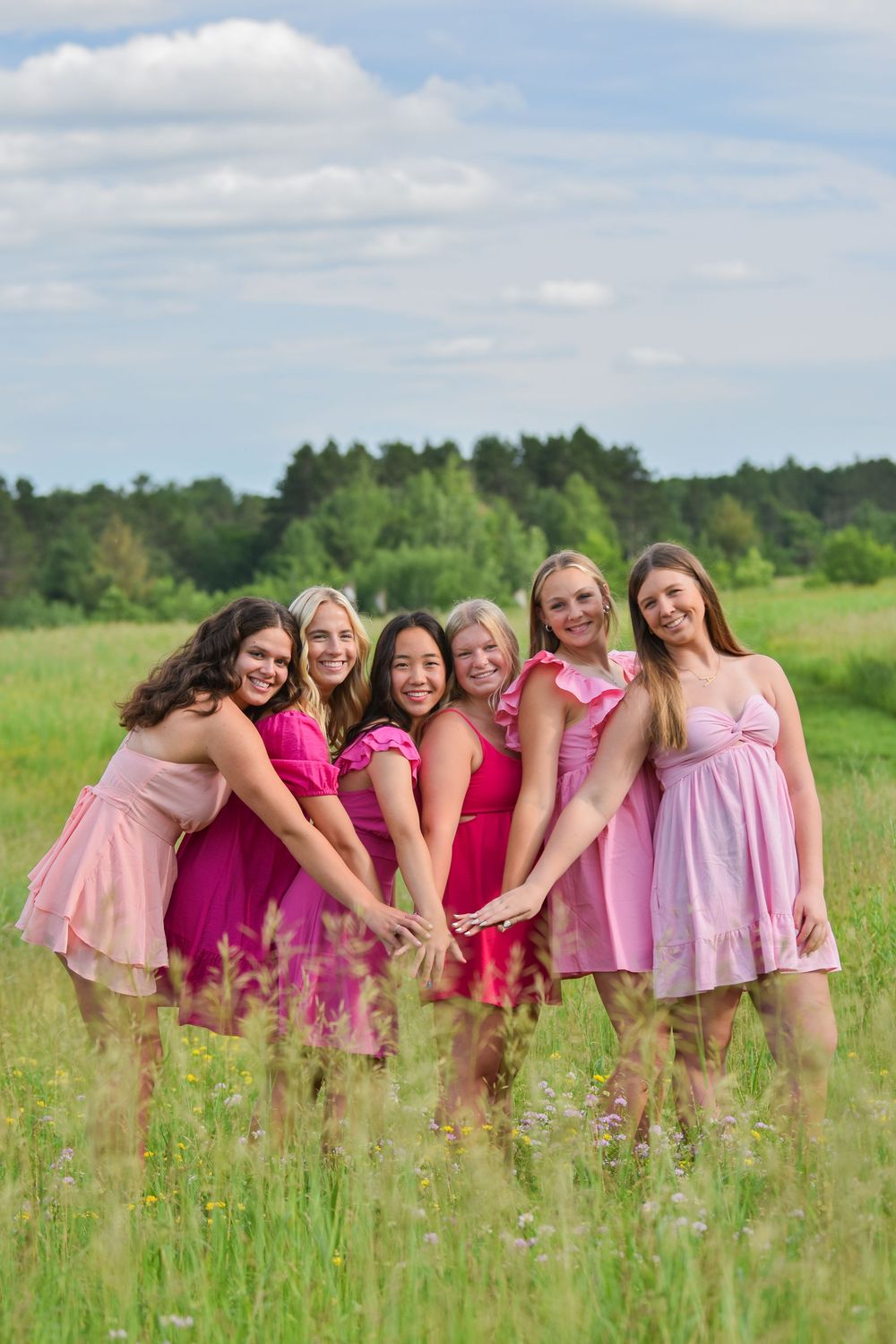 Friends in pink dresses pose together in sunny wildflower field.