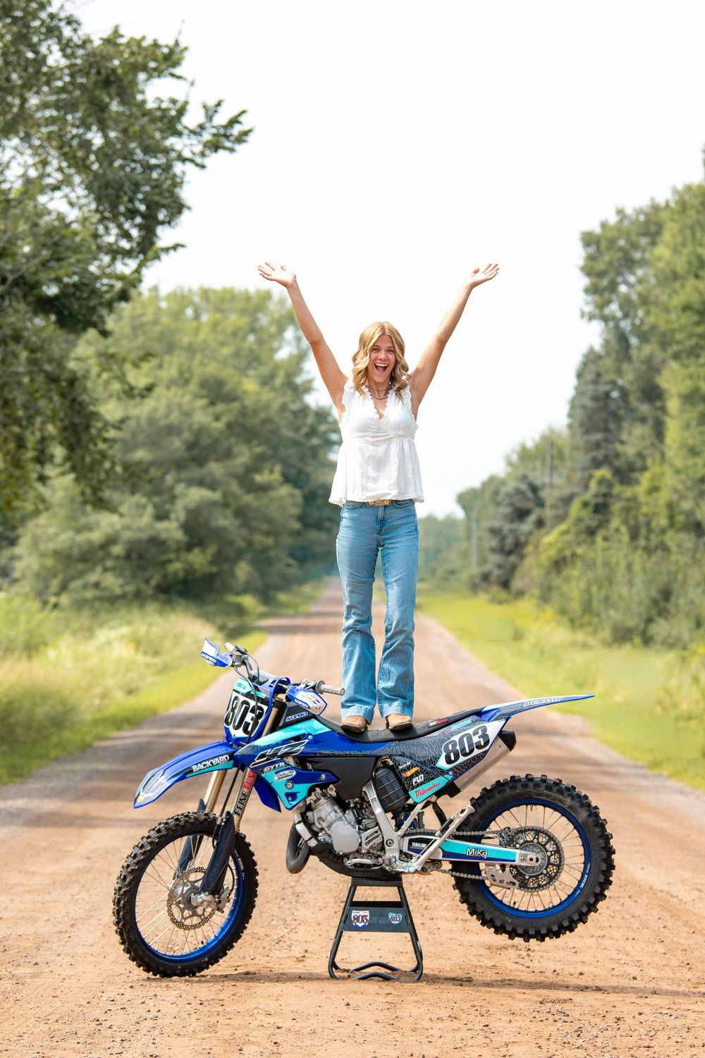 Various poses with a blue dirt bike on a rural dirt road surrounded by greenery.