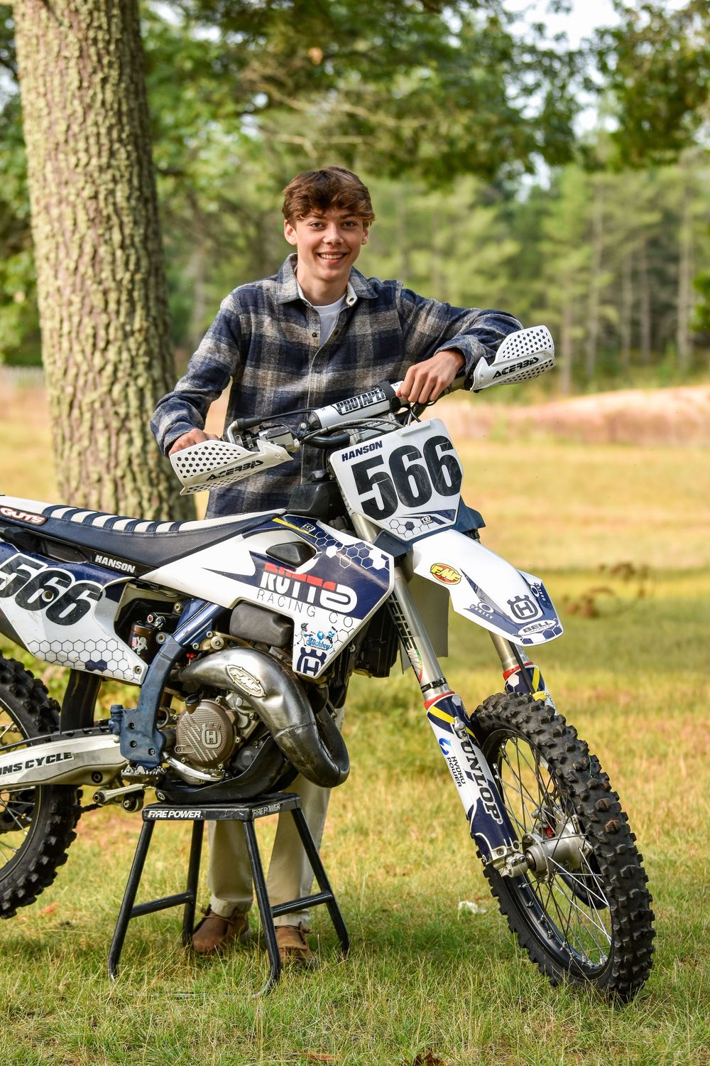 A motocross bike with racing number 566 displayed on a maintenance stand in an outdoor setting.