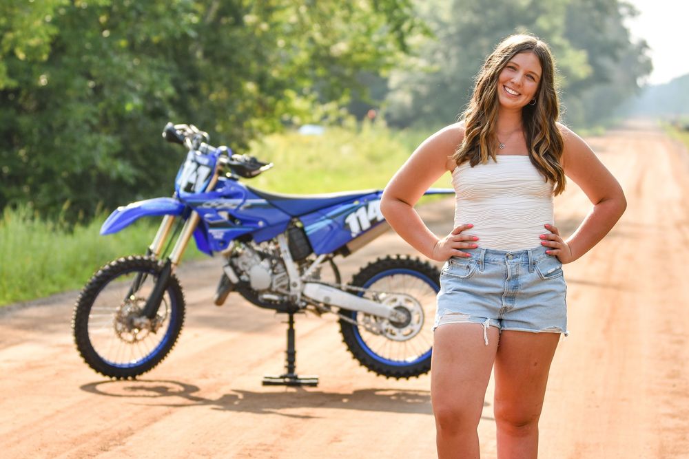 Blue dirt bike parked on dirt path with person posing beside it.