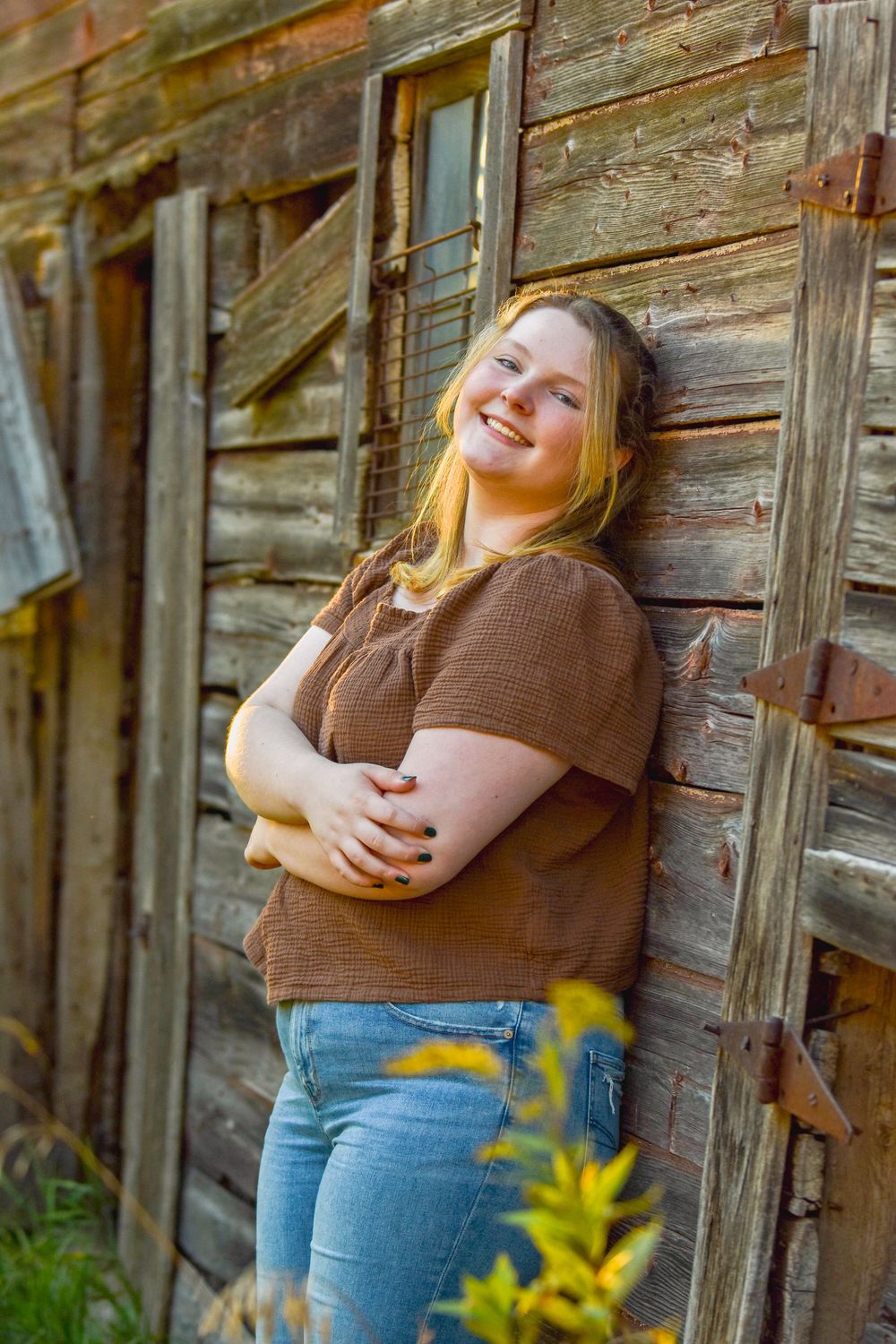 A casual portrait against weathered wooden barn walls during golden hour.
