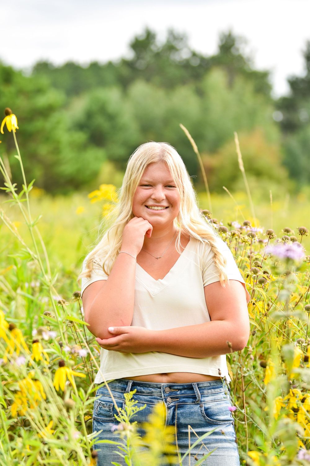 Person in white top and jeans poses in field of yellow wildflowers.