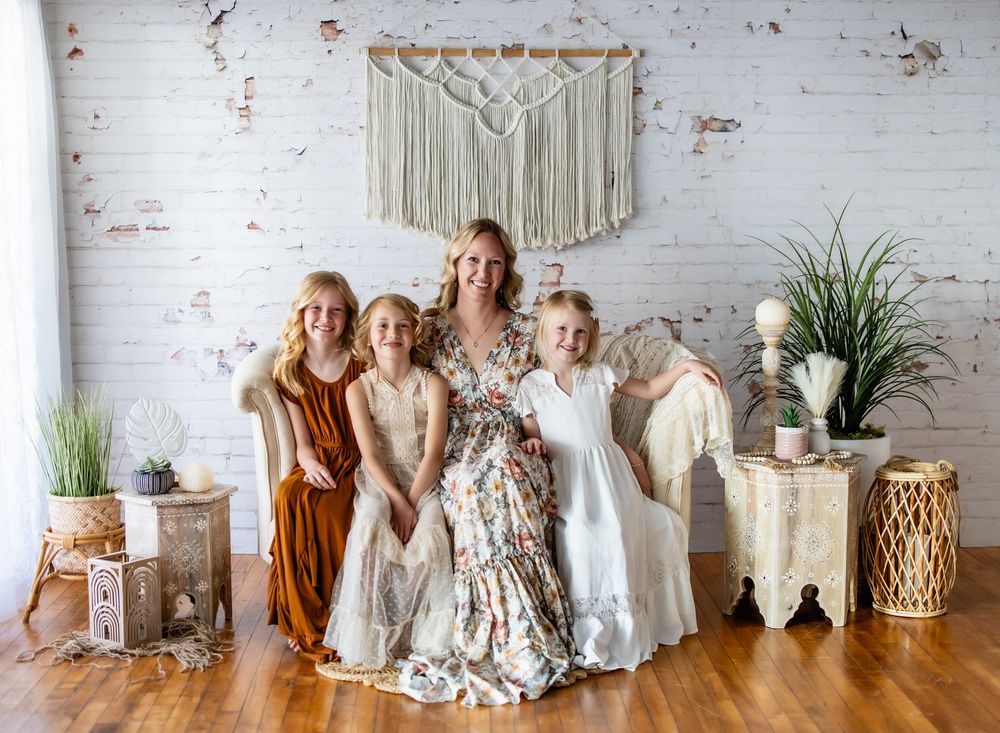 A family sits together on a wooden floor against a white brick wall with boho macrame decor and plants.