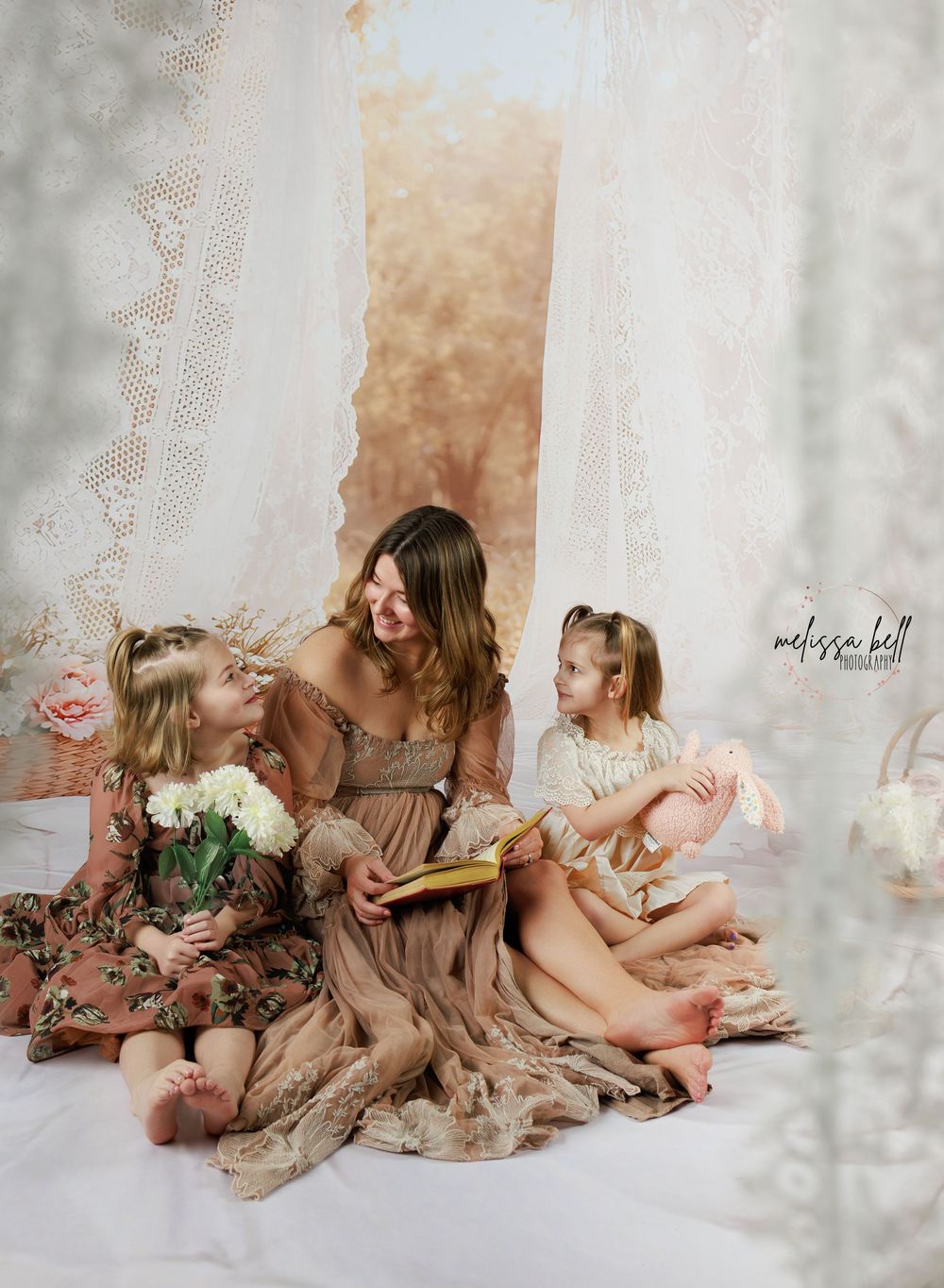 A group of children in pink and brown dresses sit together on the floor in a dreamy studio setting.