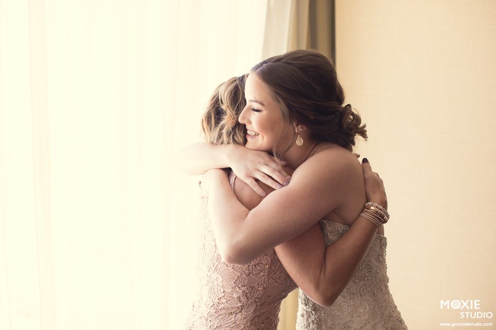Emotional embrace shared between wedding party members in burgundy and blush dresses.