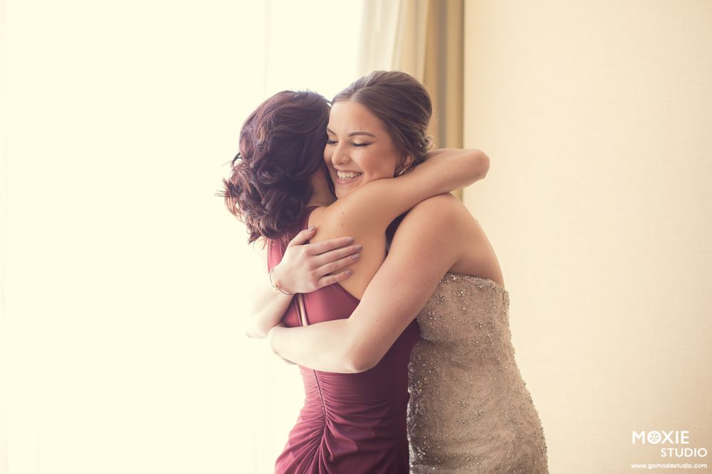 Emotional moments shared between a bride in white and bridesmaid in burgundy during wedding preparations.