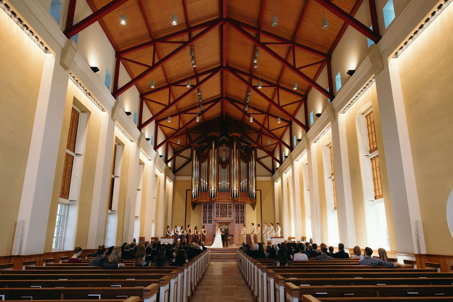 A panoramic view of a modern church interior with exposed wooden beams and white walls illuminated by natural light.