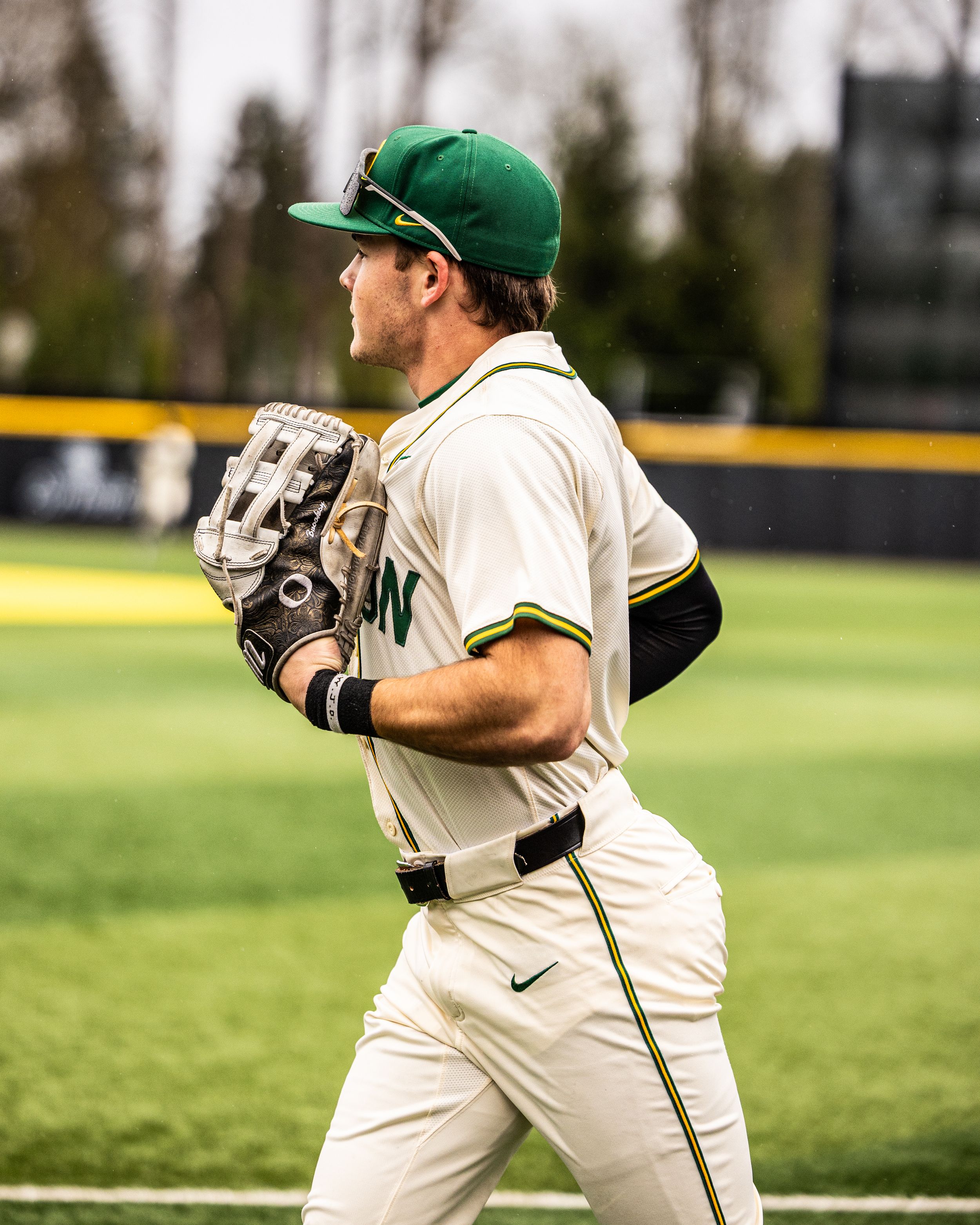 Baseball player in white uniform crouches in fielding position on grass field during game practice.