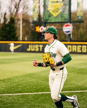 Baseball player in green and white uniform making a diving catch attempt on the field during a game.