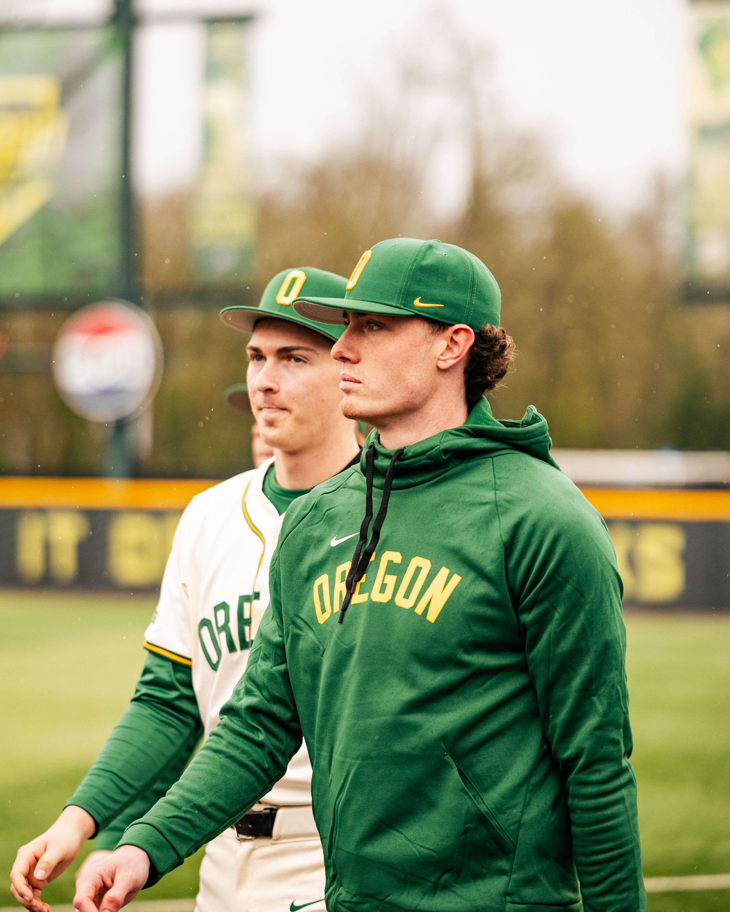 Baseball players in green Oregon uniforms gather on the field during a game.