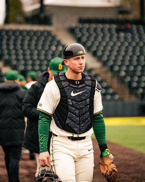 Baseball catcher in green and white uniform crouches behind home plate during a game.