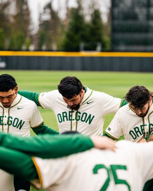Baseball players in Oregon uniforms huddle together on a field during a game.