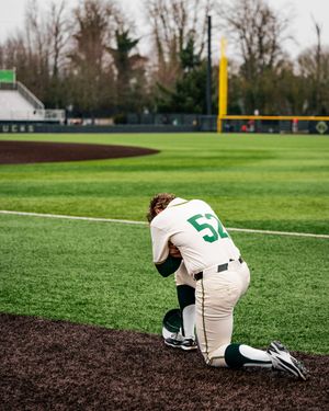 A baseball player slides into base on a dirt infield during a game on a green turf field.