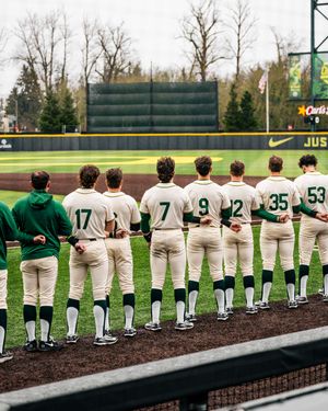 Baseball team players lined up on field wearing white and green uniforms with numbered jerseys during game.